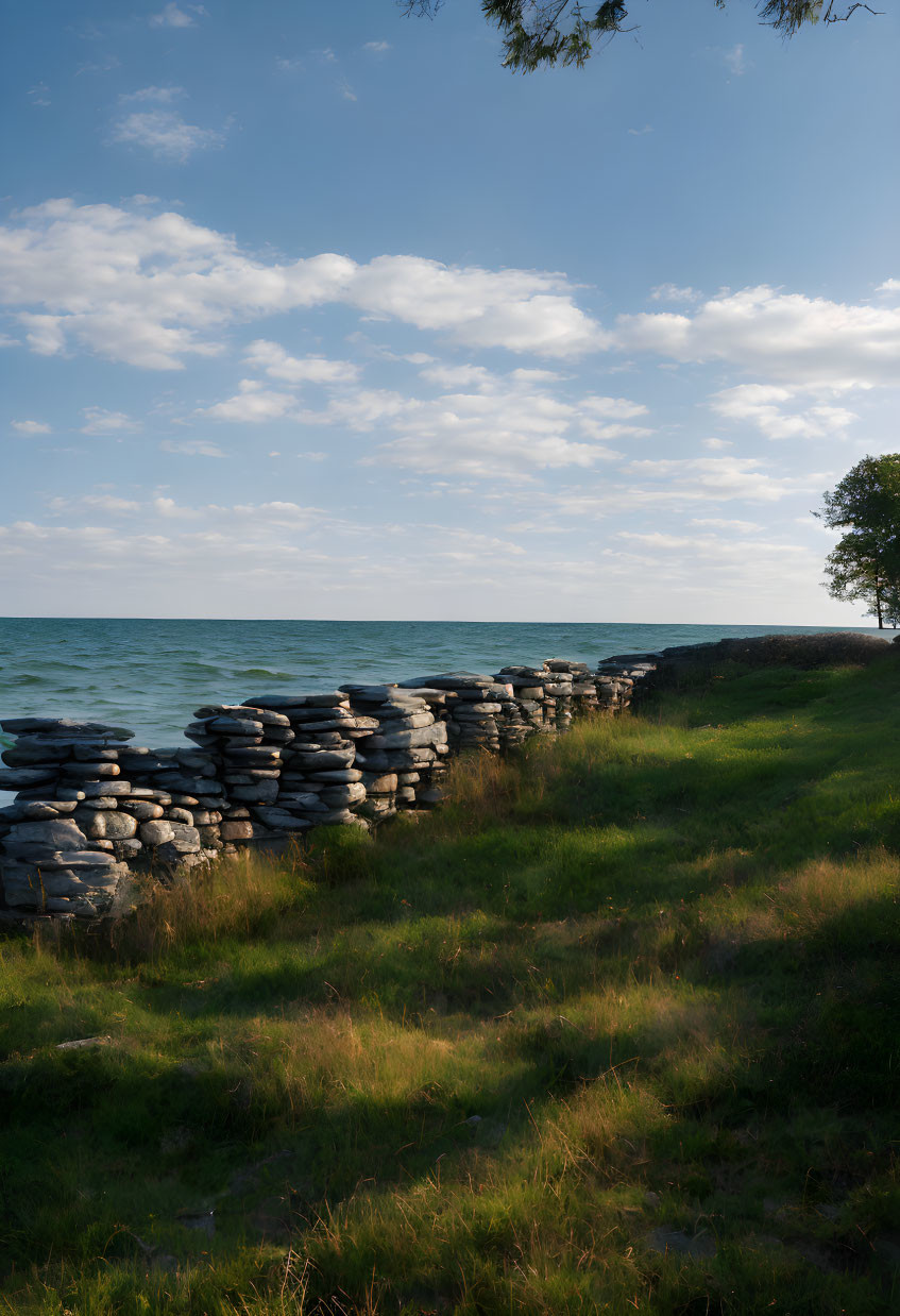 Tranquil lakeside scene with stacked stone wall, grass, trees, and blue sky