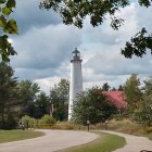 Tall white lighthouse with red cap beside house in lush greenery