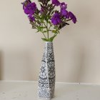 Purple and white flowers in tall elegant vase on neutral background