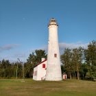 White Lighthouse with Red Top Amid Green Trees and Dramatic Sky