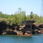 Scenic view of lush green trees on red and brown cliffs near calm blue lake