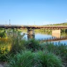 Tranquil landscape with river, arched bridge, wildflowers, and people by dock