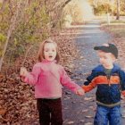 Children walking hand in hand on sunlit forest path amid autumn foliage