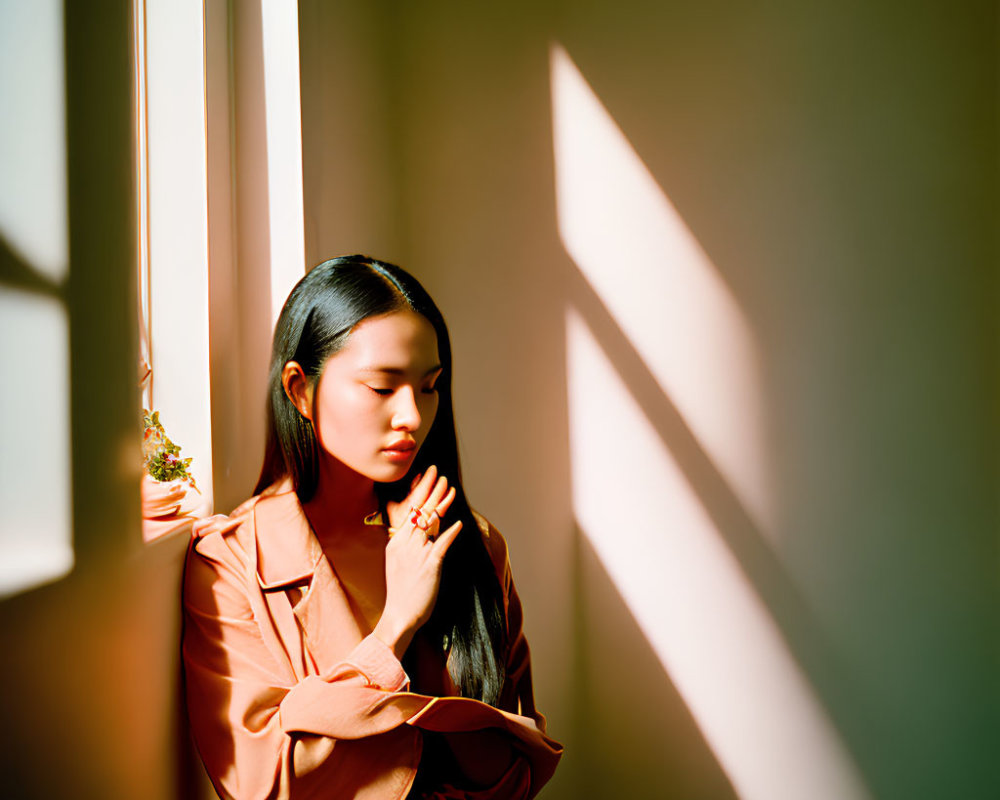 Pink-outfitted woman gazes by window with geometric shadows.