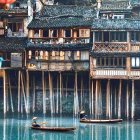 Asian stilt houses and boats on calm water at twilight.