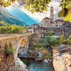 Tranquil village scene with traditional houses, river, hills, and mountains