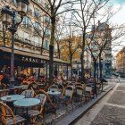 Autumn street cafe scene with vintage lamps, falling leaves, and customers.