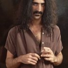 Portrait of person with long curly hair and mustache in rings on dark textured background