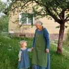 Elderly woman and young girl in matching blue dresses under tree in nature