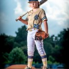 Confident young baseball player in uniform on field with bat and glove