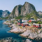 Picturesque red wooden houses on rocky coast with green hills and blue sky