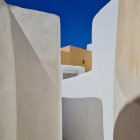 White-walled alley with blue doors, staircases, yellow dome building under blue sky