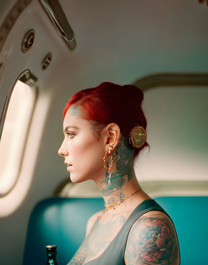 Red-haired woman with tattoos in turquoise interior gazing out window