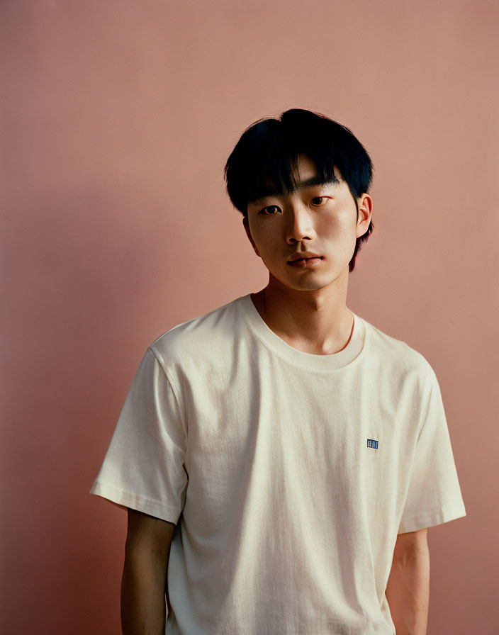 Young man in white t-shirt against pink background gazes at camera