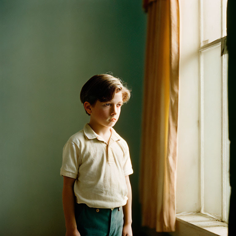 Young boy by window gazing left in warm sunlight