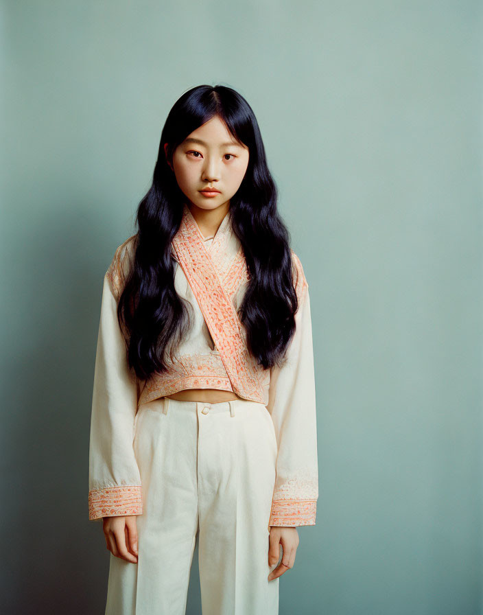 Asian woman in traditional outfit against teal backdrop