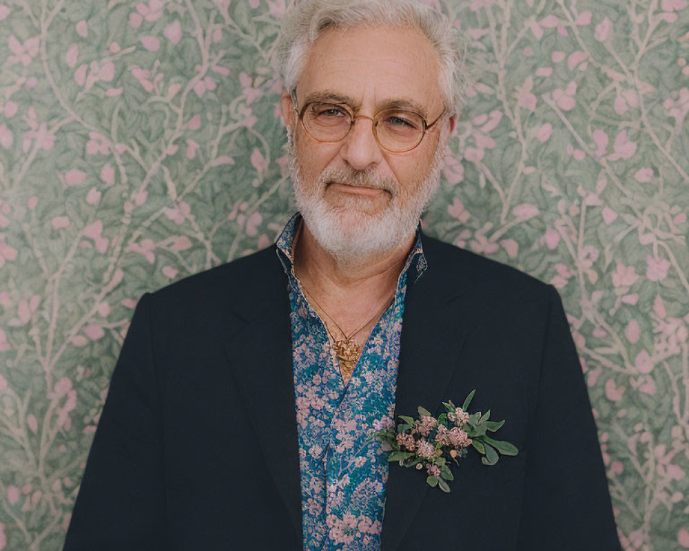 Gray-haired elderly man in glasses, blue shirt, blazer, and floral boutonniere on