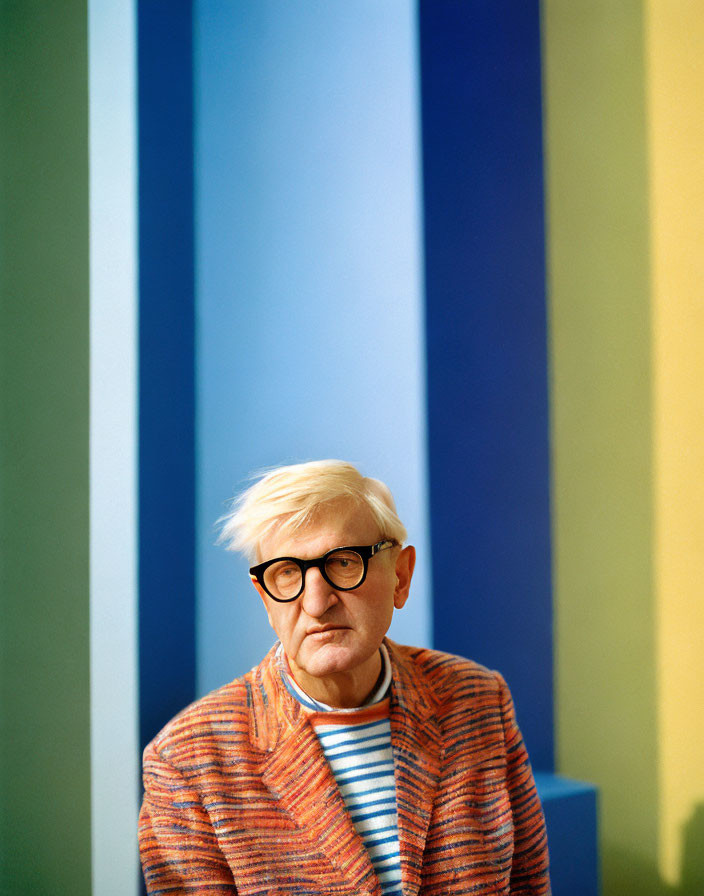 Person in Glasses with Striped Shirt and Textured Jacket against Colorful Striped Background