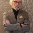 White-haired man in patterned suit with crossed arms on textured background