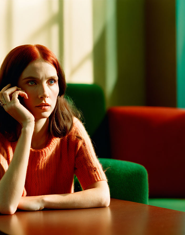 Red-haired woman in orange sweater gazes pensive under warm sunlight.