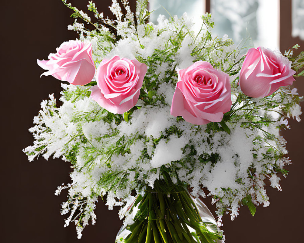 Pink roses and white baby's breath in glass vase on wooden table with window view