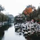 Asian village scene with historic attire, pagoda buildings, stone bridge, river, trees, and water