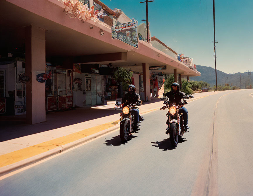 Two motorcyclists in front of vintage building under clear blue sky