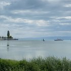 Surreal landscape with calm lake, sailboat, castle, layered clouds, crescent moon,