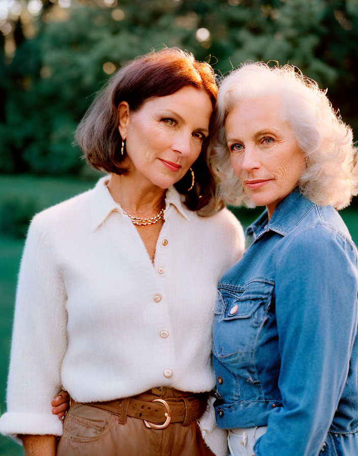 Two mature women in white sweater and denim shirt outdoors under sunlight.