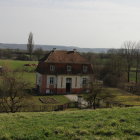 Pastoral landscape at dusk with glowing sun, large house, outbuilding, and figures in tall grass