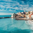 Vibrant coastal town scene with beach, buildings, sailboats, and blue sky