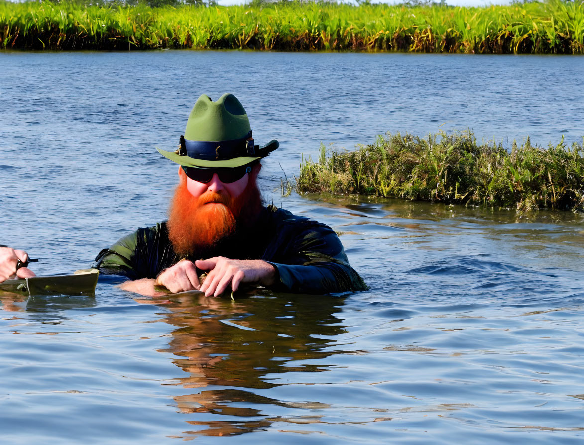 Bearded man with sunglasses and green hat in water against blue sky