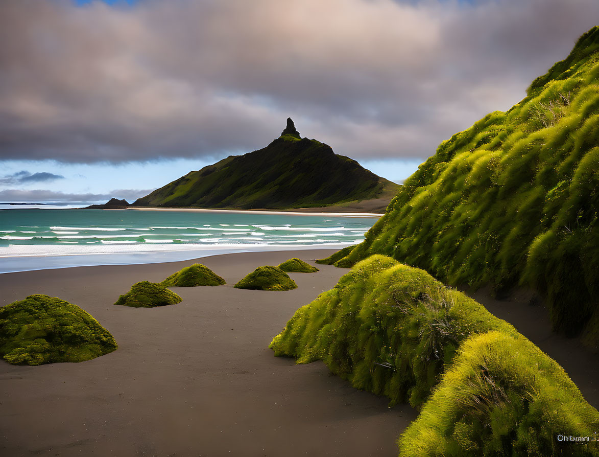 Green hillsides meet beach under cloudy sky