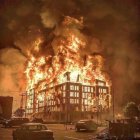 Towering Building Engulfed in Flames and Smoke on Dramatic Cloudy Sky