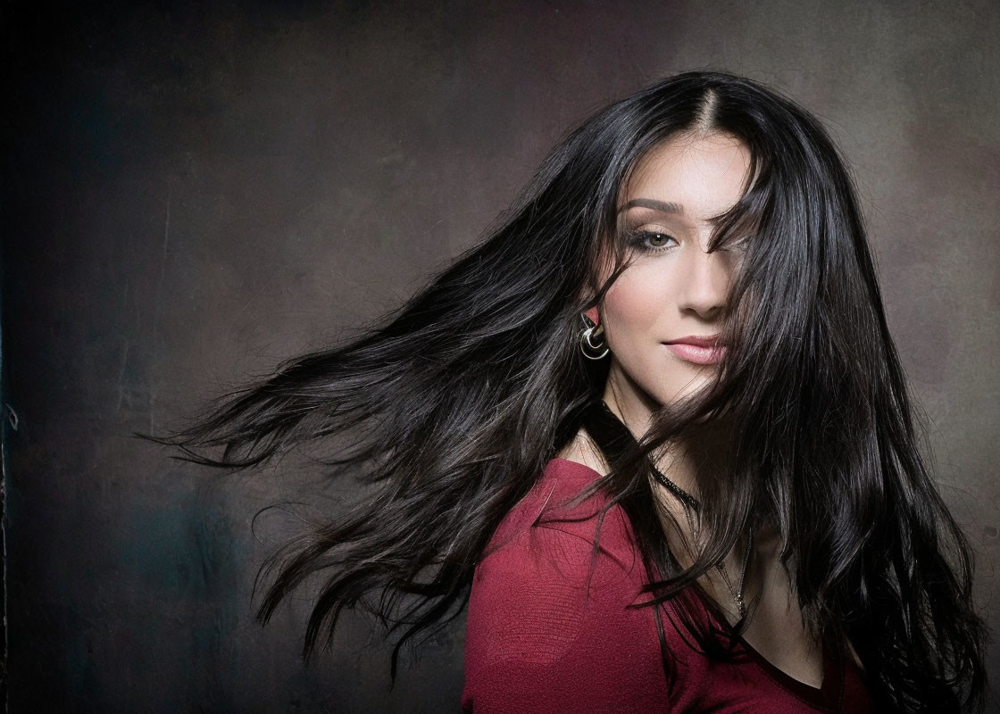 Long-haired woman in red top smiles on textured gray background