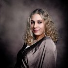 Portrait of young woman with shoulder-length curly hair in dark blouse on gray backdrop