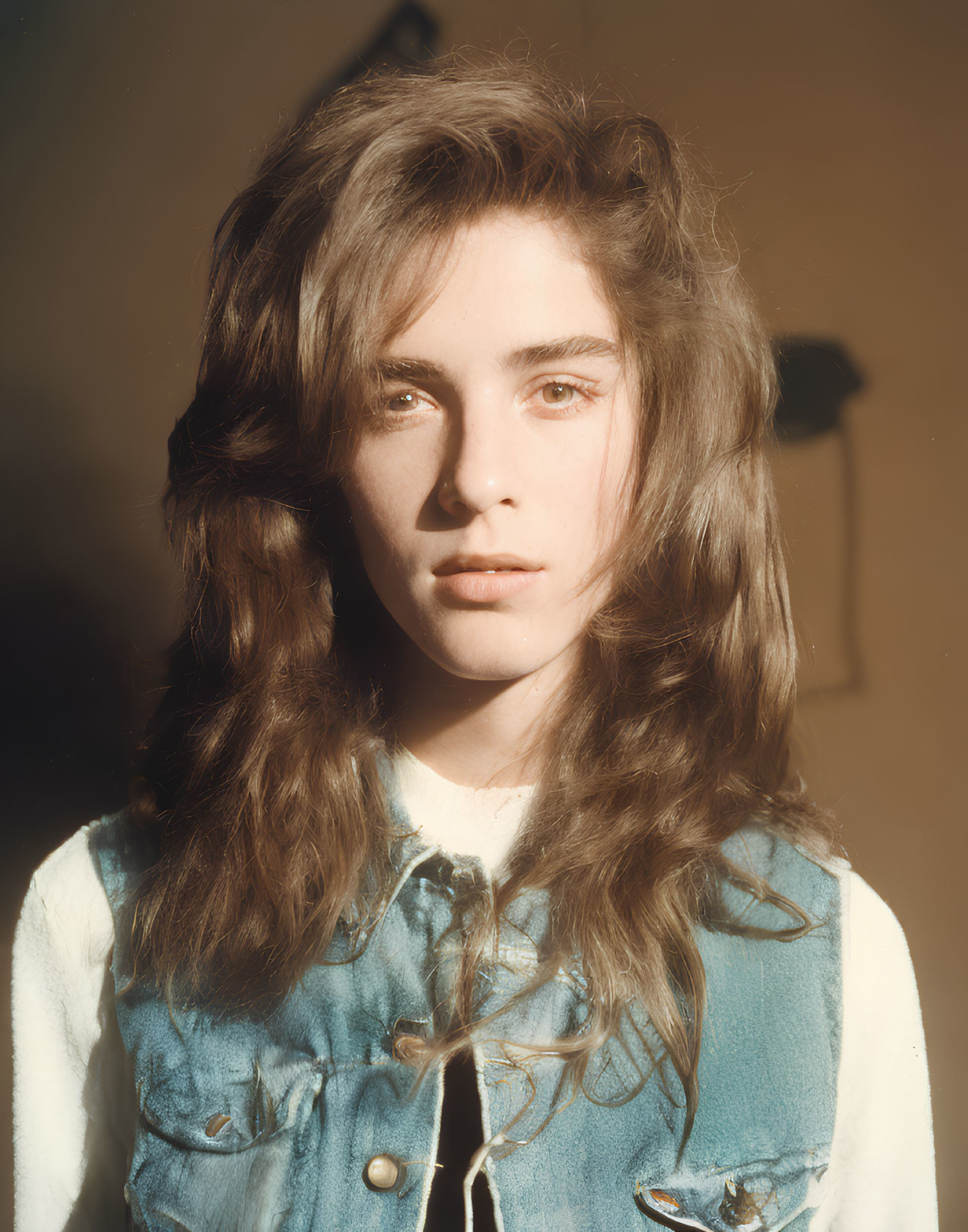 Young person with long wavy hair in denim vest under sunlight glare