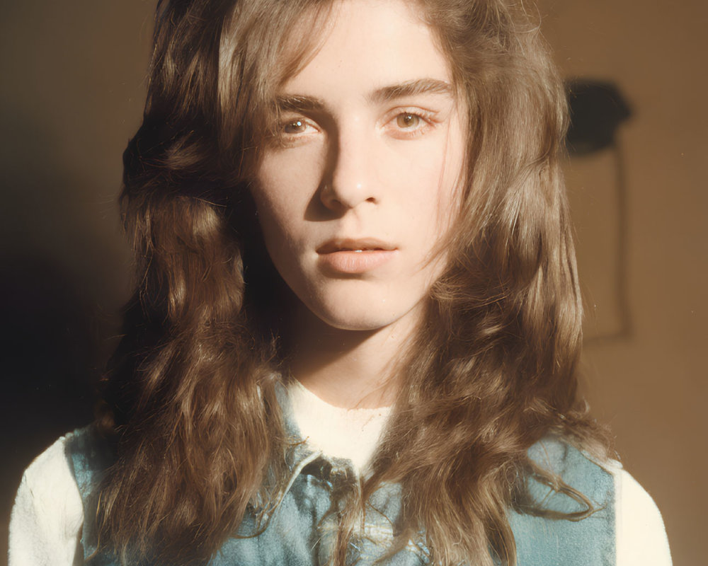 Young person with long wavy hair in denim vest under sunlight glare