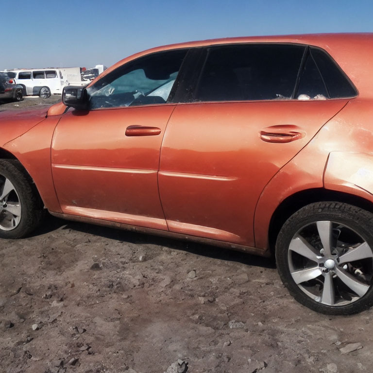 Orange glossy car parked on dusty ground under clear blue sky