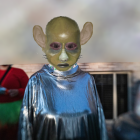 Green-skinned alien in blue robe with red berries background