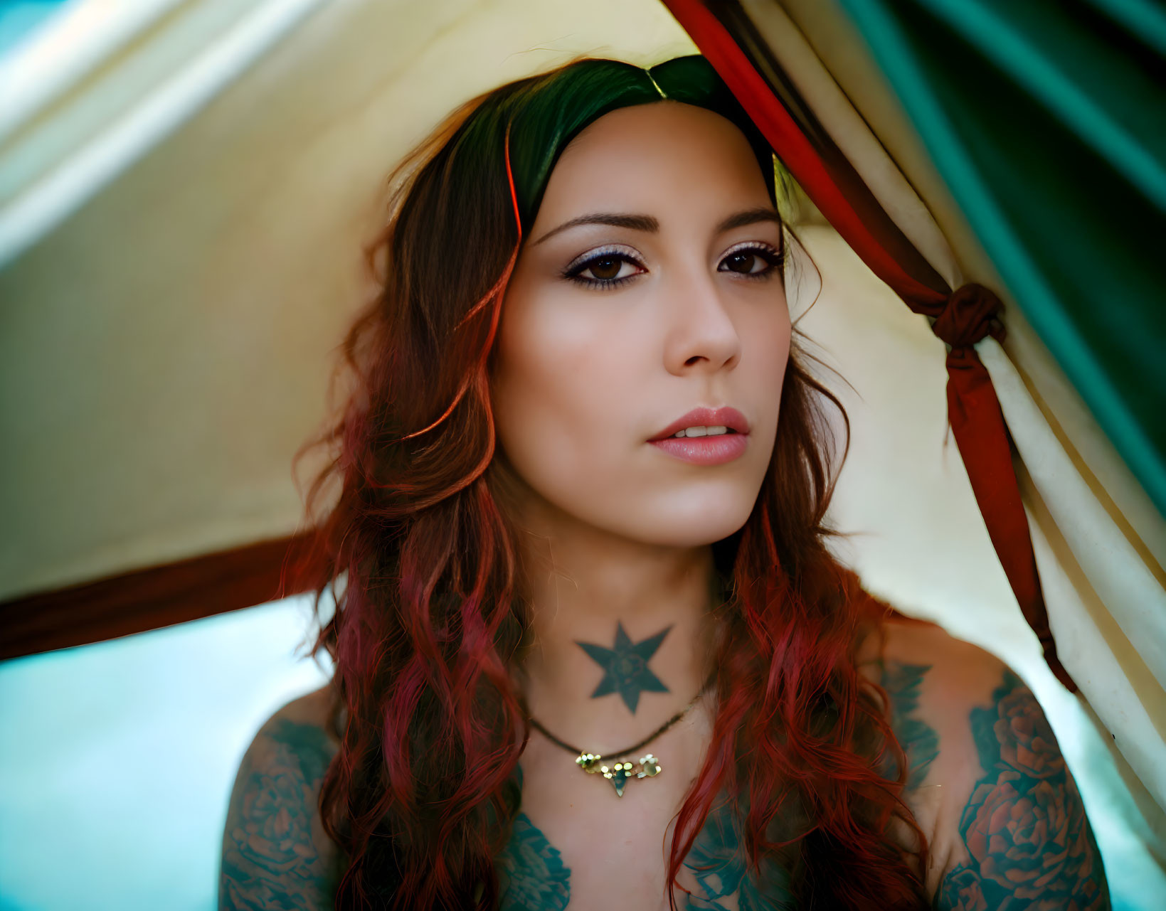 Red-haired woman with tattoos and headband under colorful canopy.