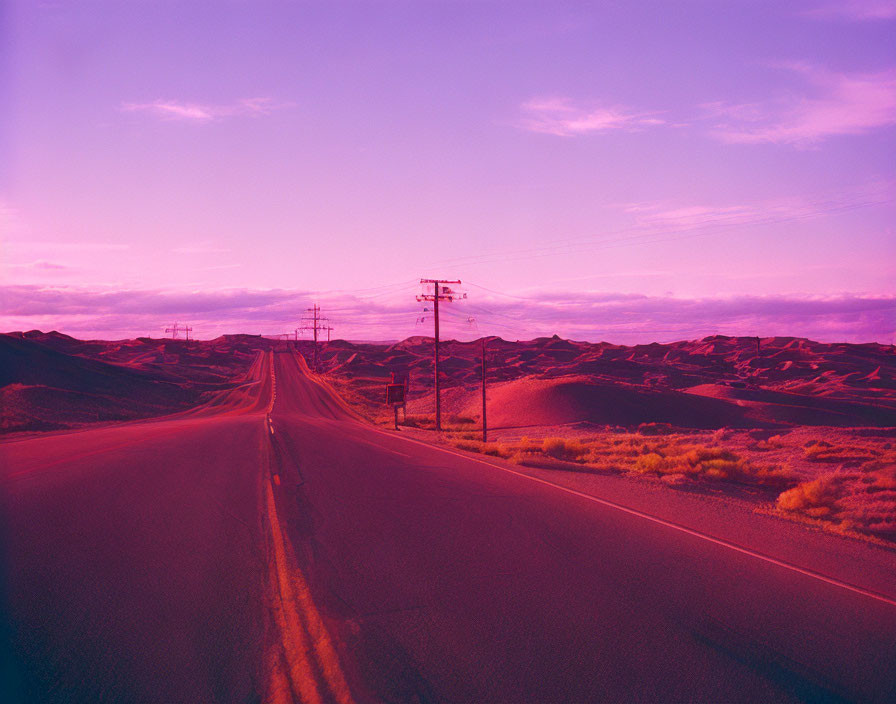 Desert road at sunset with purple hue and rolling dunes