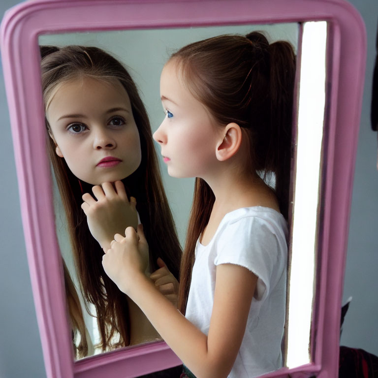 Young girl with ponytail gazes at reflection in pink-framed mirror