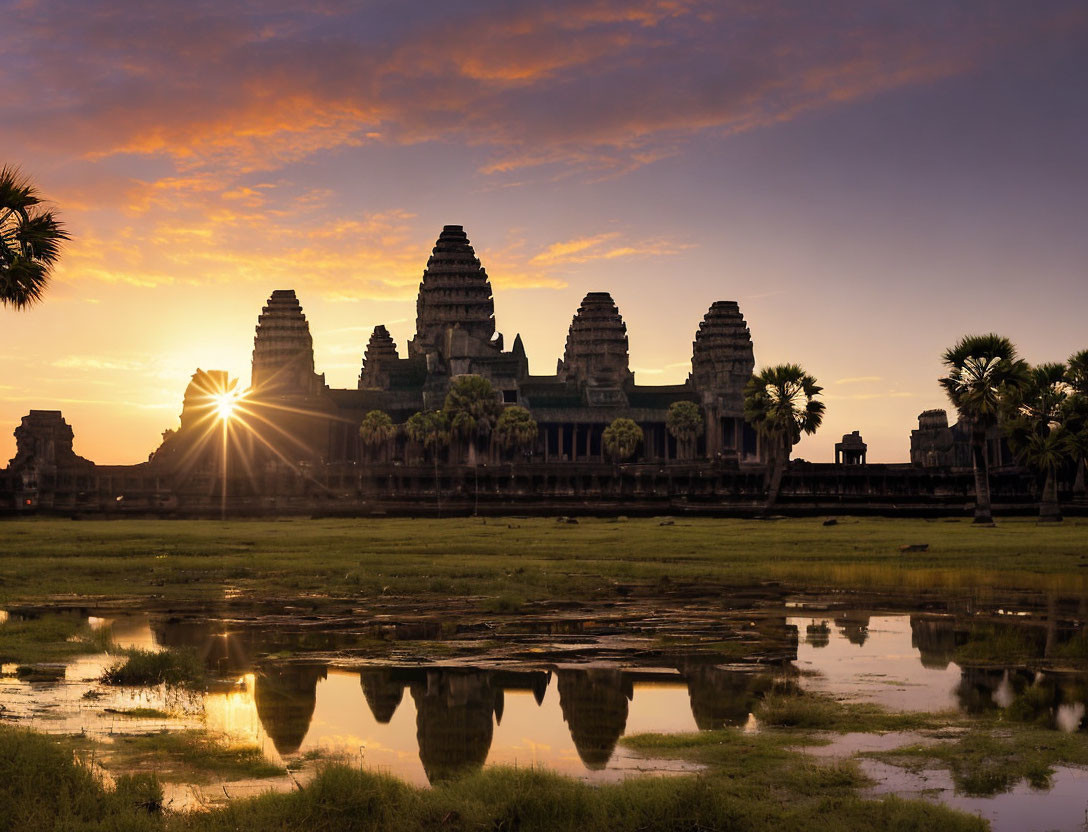 Ancient Angkor Wat temple at sunrise with palm tree silhouettes and golden sky