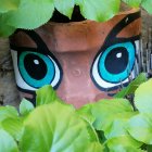 Colorful face in green leaves with blue eyes and red lips.