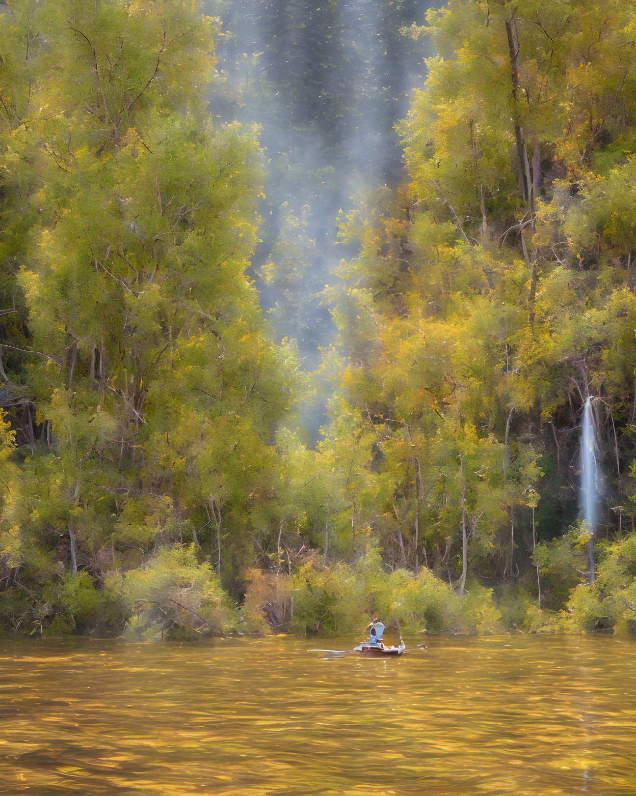 Tranquil kayaker on golden river with misty trees