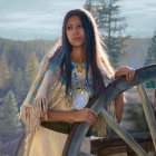 Traditional Native American Woman Beside Wooden Wheel in Forest Setting