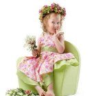 Young girl in floral dress holding flowers on green chair