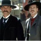 Two Men in Western Attire with Mustaches and Black Hats in Old Town Setting