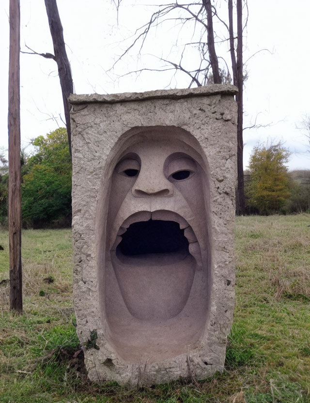 Stylized stone sculpture of surprised human face in grassy field